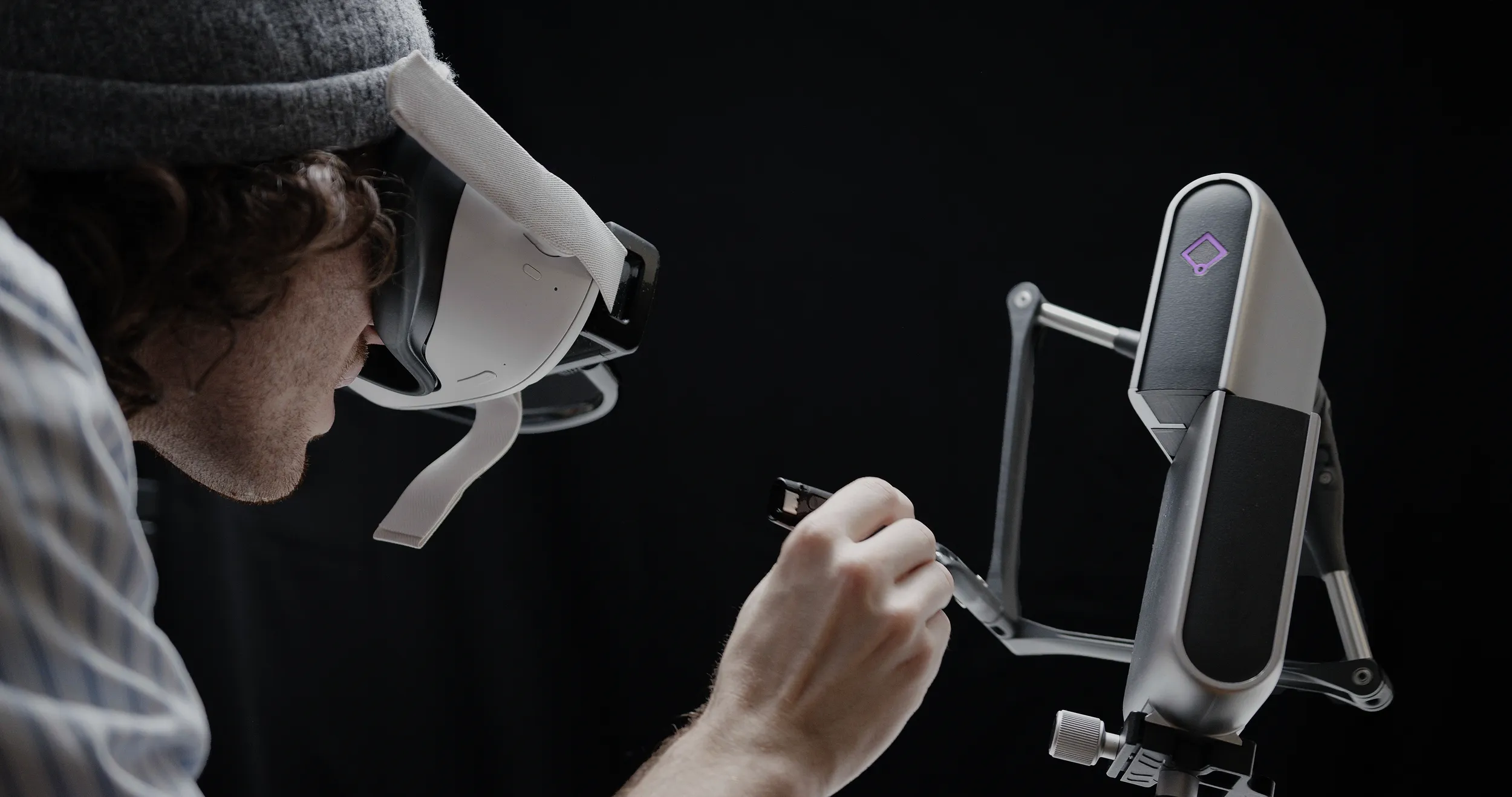 Engineer in a VR headset guiding the Inverse3 with its stylus in a dark studio, the device's diamond logo glowing purple