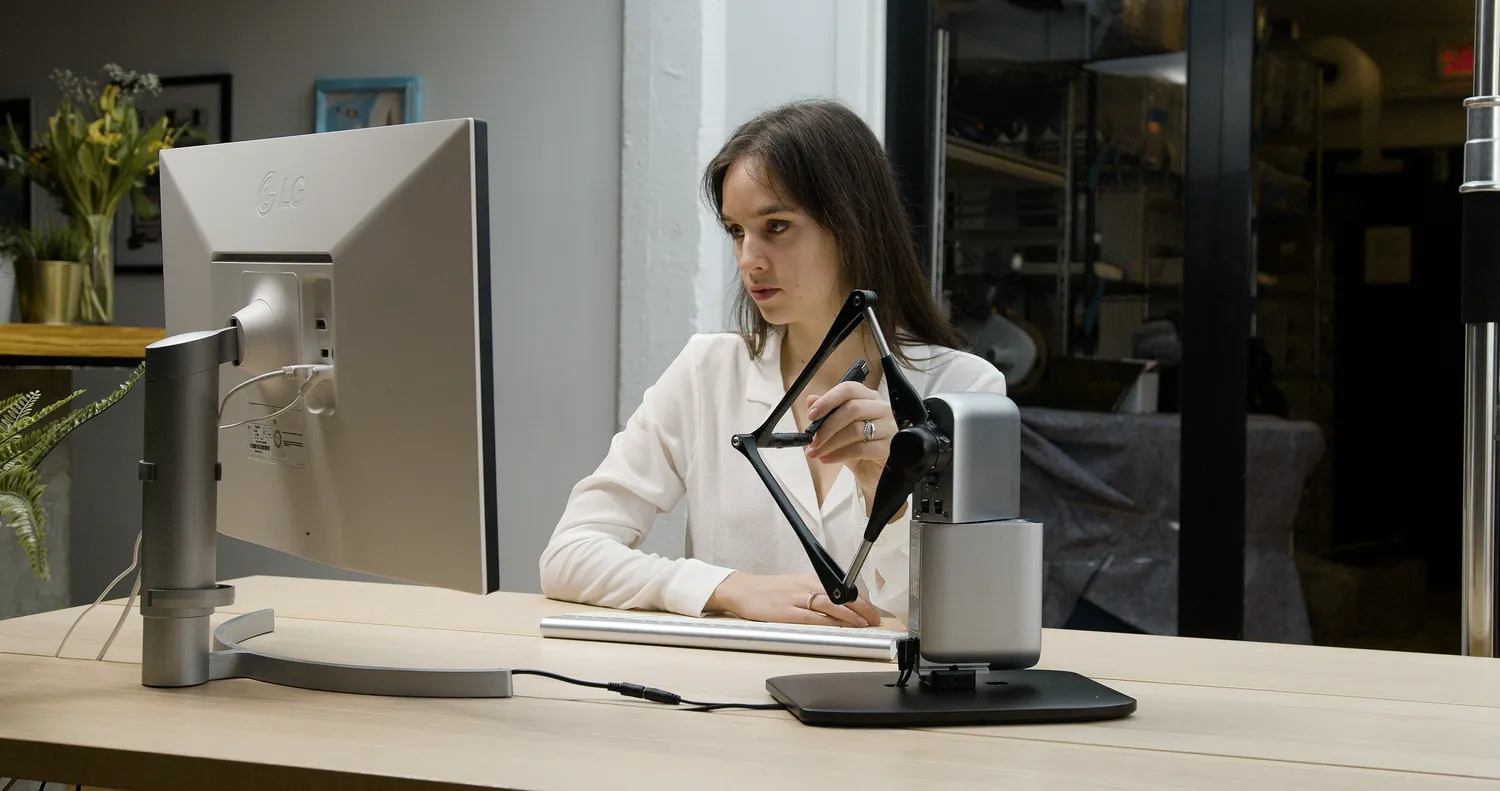 Researcher operating the Inverse3 haptic device at a desk in a workshop lab