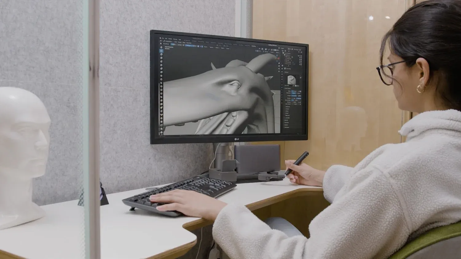 Designer sculpting a 3D head model on screen using a haptic stylus at a studio desk